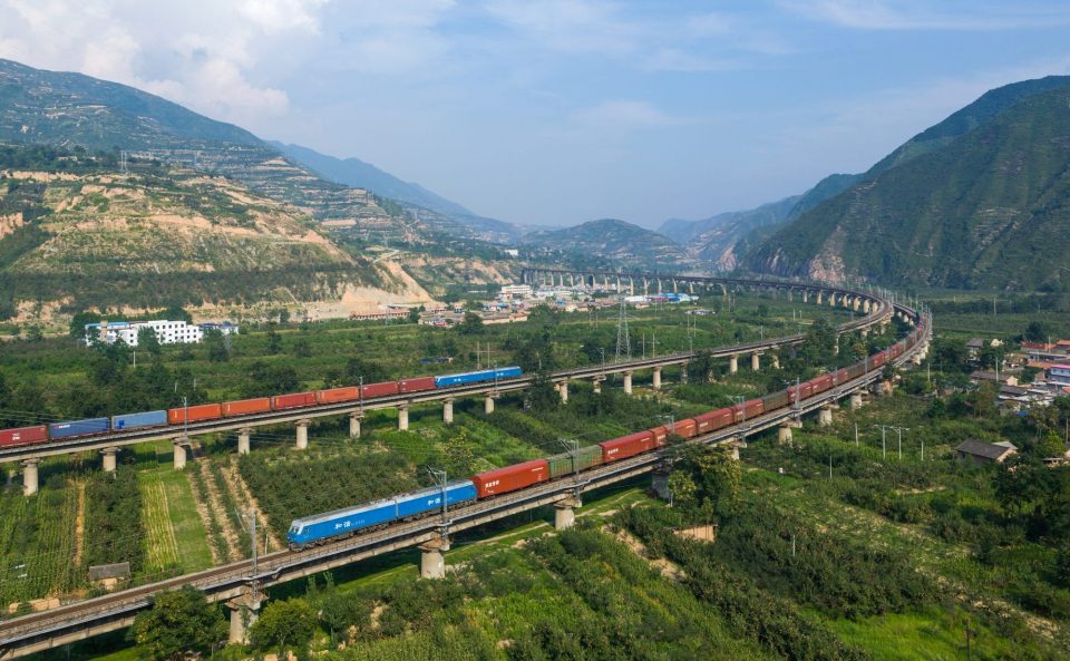 Tågräls som går över grönt landskap för tågfrakt genom Kina och Europa.